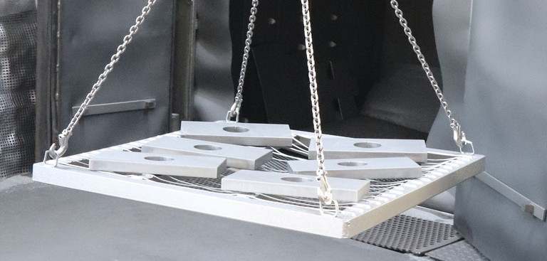 Gestrahlte Teile werden auf einem Gitter aus der Anlage transportiert